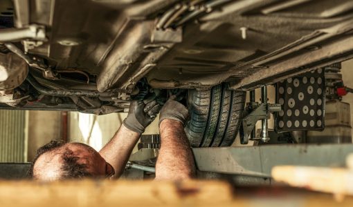 Man in a hole under a car fixing steering alignment in a garage