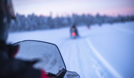 Snowmobiling on the frozen lake at sunset at Torassieppi, Lapland, Finland